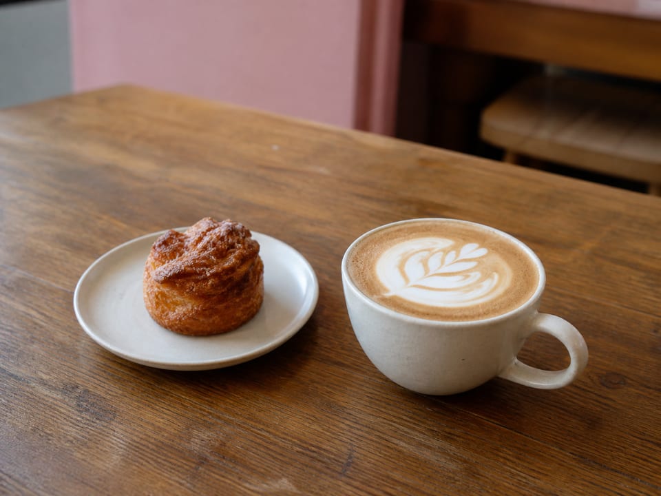 Café con espuma dibujada y una pieza de bollería artesanal