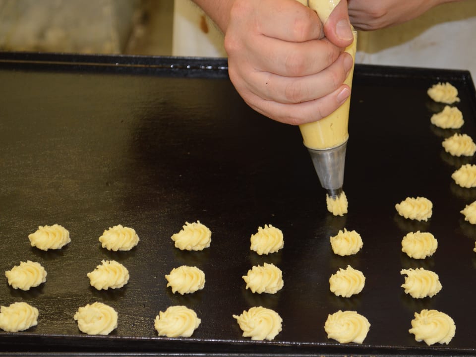 Pastelero dando forma con manga a pequeñas pastas en el obrador